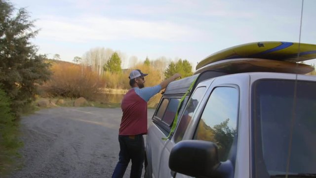 Man takes his paddle board off his truck and heads towards the river 