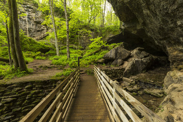 Fototapeta premium Bridge To Cave / A footbridge crossing a stream and leading towards a cave entrance.