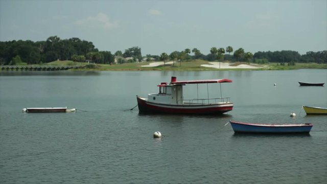 A few colorfully painted boats moored in a quiet lake on a sunny day with golf course greens and sand traps in the distance.