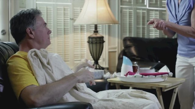 A woman brings her sick husband a tray of items he needs  explains something to him  then exits the scene.