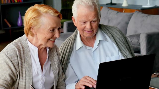 Senior couple websurfing on internet with laptop. Happy elderly man and woman using computer