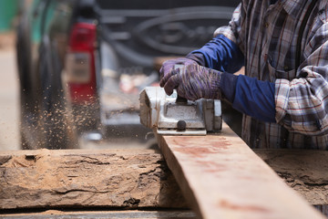 worker planing a wood with a electric plane