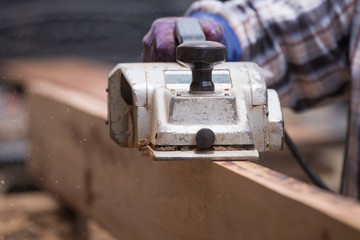 worker planing a wood with a electric plane