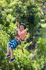 Naklejka na ściany i meble Happy smiling little boy riding a zip line in a lush tropical forest