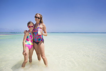 Beautiful Woman and her cute daughter enjoying a fun day while on a tropical beach vacation. Woman is drinking a pina colada drink.