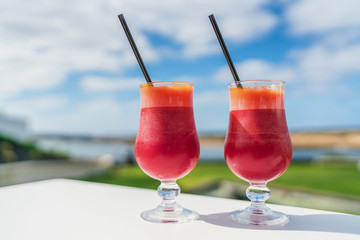 Healthy eating juice cleanse detox concept. Vegan diet juicing trend. Two glasses of red vegetable blend of carrot, beet juices glasses on outdoor cafe or restaurant table on summer sky background.