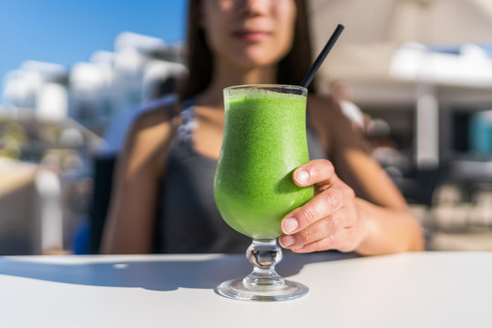 Healthy juicing lifestyle trend woman drinking green spinach juice smoothie cup at restaurant table. Unrecognizable person holding glass of fresh vegetables blend for a vegetarian diet detox cleanse .
