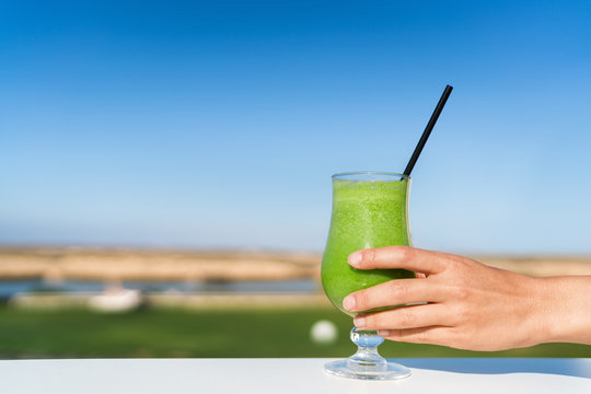 Woman Holding Green Smoothie Glass Drinking Fresh Cold Pressed Organic Vegetable Spinach Juice Outside At Cafe Table. Healthy Eating Diet Juicing Cleanse Detox. Unrecognizable Person Reaching For Cup.