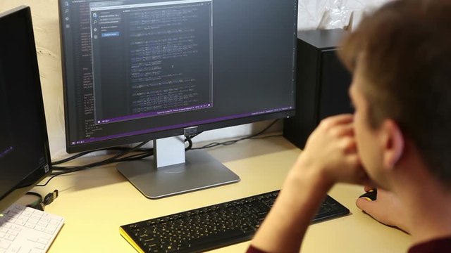 young guy programmer typing on a keyboard code. back view. Focus on the screen.