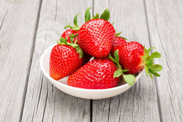Fresh ripe strawberries in a simple white bowl, on gray wooden table