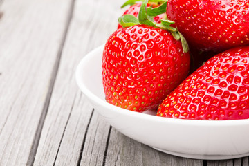 Fresh ripe strawberries in a simple white bowl, on gray wooden table