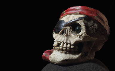 Cráneo de pirata con pañoleta roja, ojo tapado y arete de oro sobre un fondo oscuro.