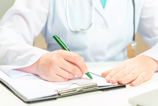 Doctor in a white coat writes on a paper prescription