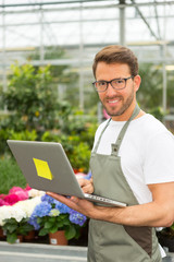 Fototapeta premium Young attractive man working at the plants nursery using laptop