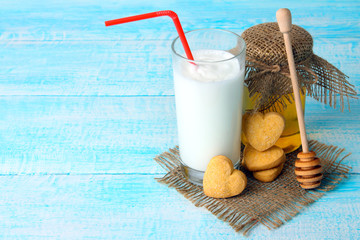 a milkshake with a cocktail straw near the jars of honey and honey spoon by the biscuits on sackcloth on wooden background