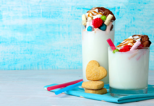 a milkshake with a cocktail straw and biscuits with chocolates on a napkin on wooden background