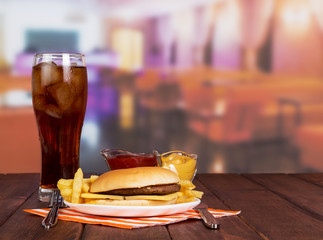 Hamburger, french fries, glass cola, sauces  in  background  hall cafe.