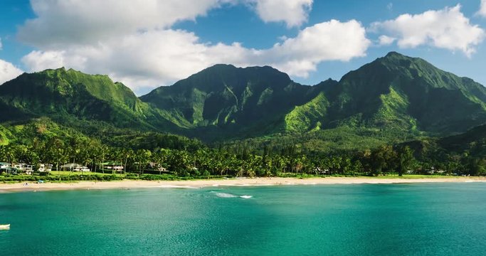 Aerial view flying over tropical blue ocean towards beautiful green mountains and white sandy beach. Hanalei Bay, Kauai