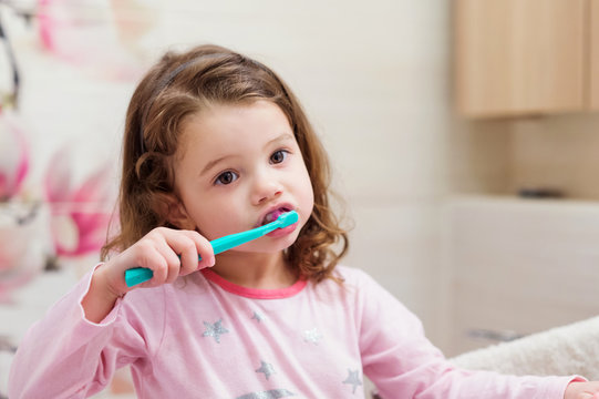 Little girl in pink pyjamas in bathroom brushing teeth