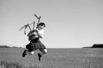 Black white photography of man jumping high with pipes in Scottish traditional kilt on summer field...
