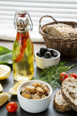 Mussels and black olives and in ceramic bowls, fresh tomatoes, sliced lemon, bread and bottle of olive oil with spices on black stone board. Mediterranean food on black stone board
