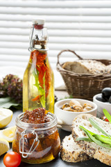 Dried tomatoes in jar and bottle of olive oil with spices, mussels and black olives and in ceramic bowls, bread, fresh tomatoes, sliced lemon, herbs on black stone board. Mediterranean food