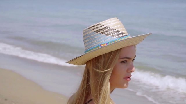 Pensive young woman in a sunhat at the seaside standing staring out over the calm ocean with a serious thoughtful expression  closeup profile view