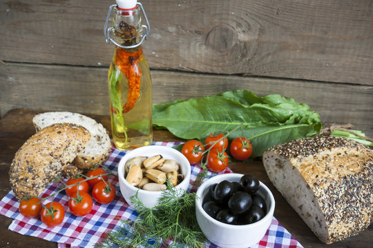 Black olives and mussels in ceramic bowls, fresh tomatoes, bread and bottle of olive oil with spices on wooden board. Mediterranean food on dark wooden background