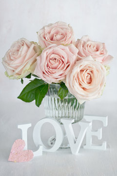 Pink roses flowers in a vase and letters "love". Floral gift for a wedding or birthday.