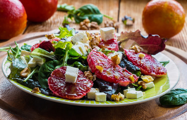 Salad: mix of green salad, feta cheese, red oranges and walnuts. Dressing: olive oil. Selective focus.