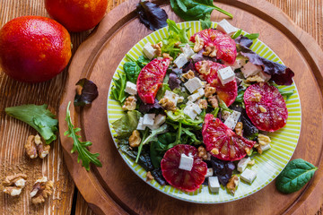 Salad: mix of green salad, feta cheese, red oranges and walnuts. Dressing: olive oil. Selective focus, top view.