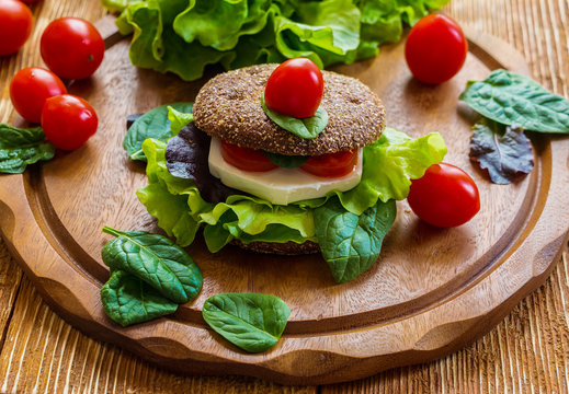 Burger: vegan burger with lettuce, fresh cherry tomatoes and feta cheese on wooden background.