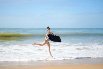 Fototapeta na wymiar Joyful surfer girl happy cheerful running surfing at ocean beach water. Female bikini heading for waves with surfboard 