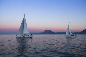 Fototapeta premium Sail boats near the rocky shores after amazing sunset.