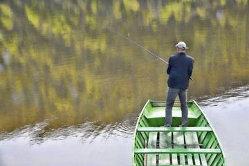 Scene Of Fisherman With His Back Towards Camera Fishing From The Boat On The Calm Lake, Water...
