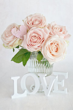Pink roses flowers in a vase and letters "love" .Floral gift for a wedding or birthday.