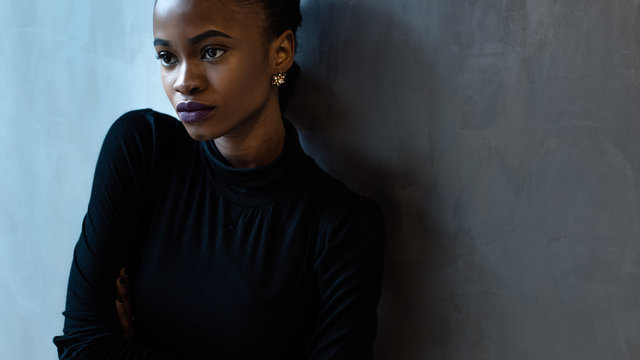 Portrait Of A Serious African Or Black American Woman With Arms Folded Standing Over Gray Background And Looking Away