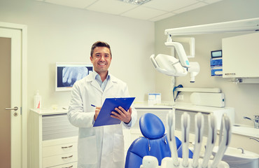 happy male dentist with clipboard at dental clinic