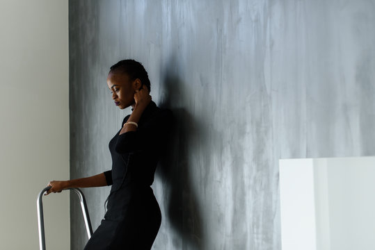 Side view of pretty african or black american woman touching her thick plait on dark studio background