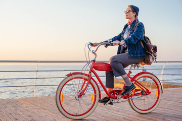 Fototapeta na wymiar woman riding red vintage bicycle on seaside during sunset or sunrise 