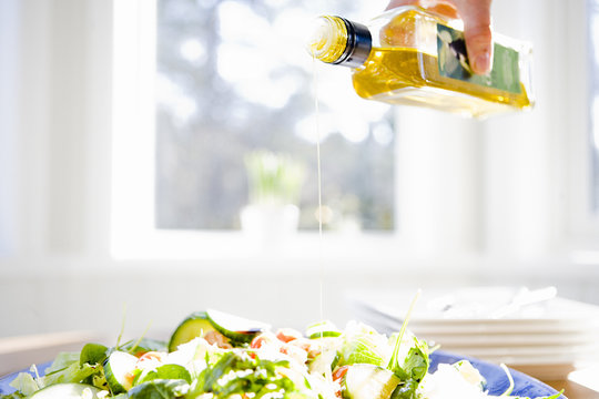 A peson pouring olive oil on a salad, Sweden.