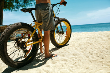 Summer Beach Sport. Close Up Of Man Legs Riding Yellow Sand Bicycle At Tropical Seaside. Fitness Male Model Exercising With Bike On Holiday Travel Vacation. Sporting Activity, Active Lifestyle Concept