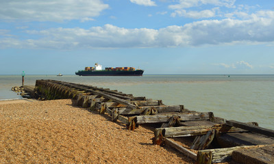  A small Container ship entering the Port of Felixstowe being guided by tug, old breakwater in foreground.
