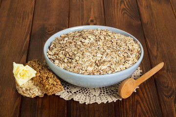 Bowl  oatmeal, bar, rose and spoon on dark wooden background.