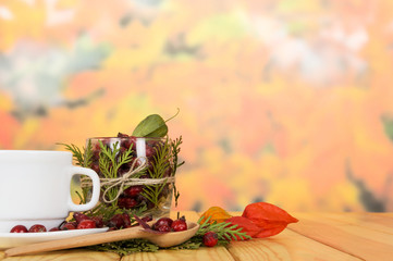 Hips, tea cup and wooden spoon on  background autumn leaves.