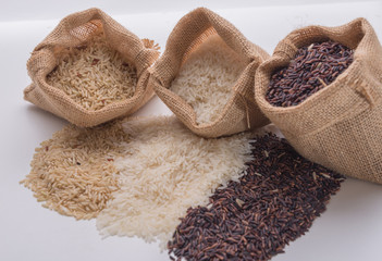 Three sack with different types of rice: brown rice, riceberry rice and white (jasmine) rice on white background. Selective focus