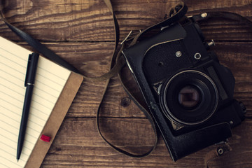 old retro camera with lined notebook and pen on  wooden background. top view - obrazy, fototapety, plakaty