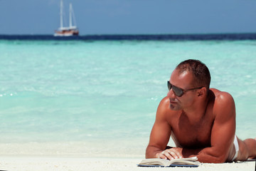handsome man reading book at the white sand beach