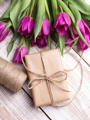 Gift box and tulips bouquet on white wooden background - retro style