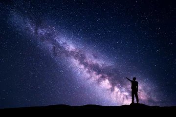 Papier Peint photo Nuit Voie lactée avec la silhouette d& 39 un jeune homme debout pointant le doigt dans le ciel étoilé de la nuit sur la montagne. Paysage de nuit. Bel univers, fond de voyage avec un ciel violet plein d& 39 étoiles